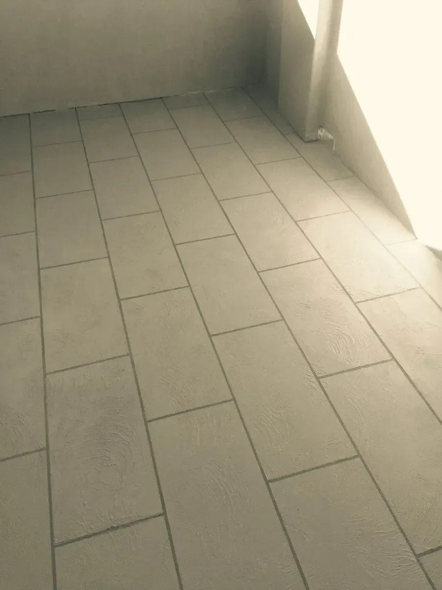 Light gray rectangular tiles on a floor, partially lit by sunlight from a window on the right.