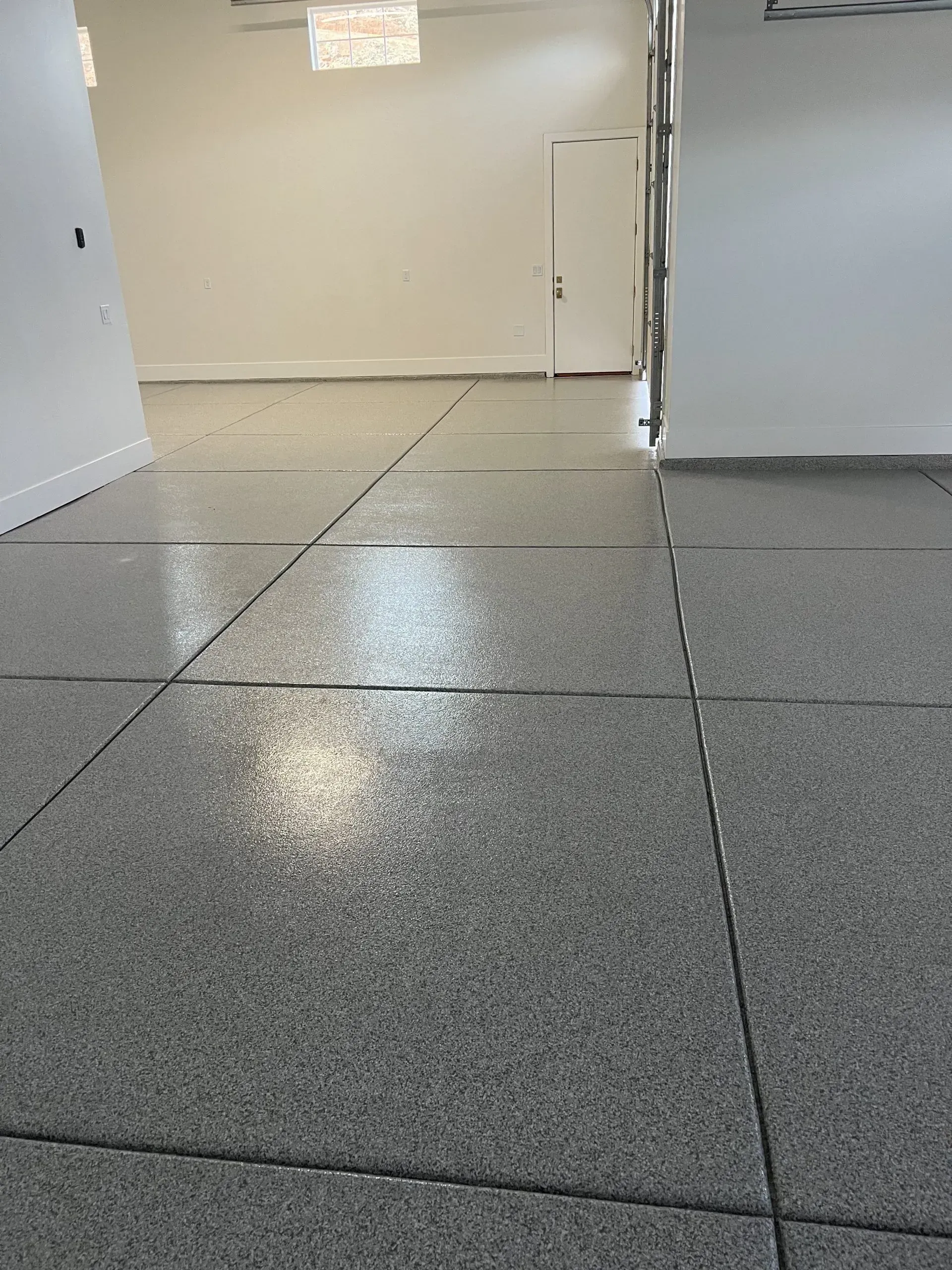 Shiny, speckled gray epoxy floor in an empty, white-walled room with visible expansion joints.