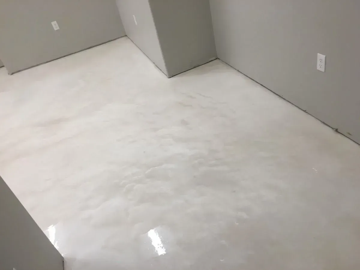 White epoxy floor in a room with gray walls and electrical outlets.
