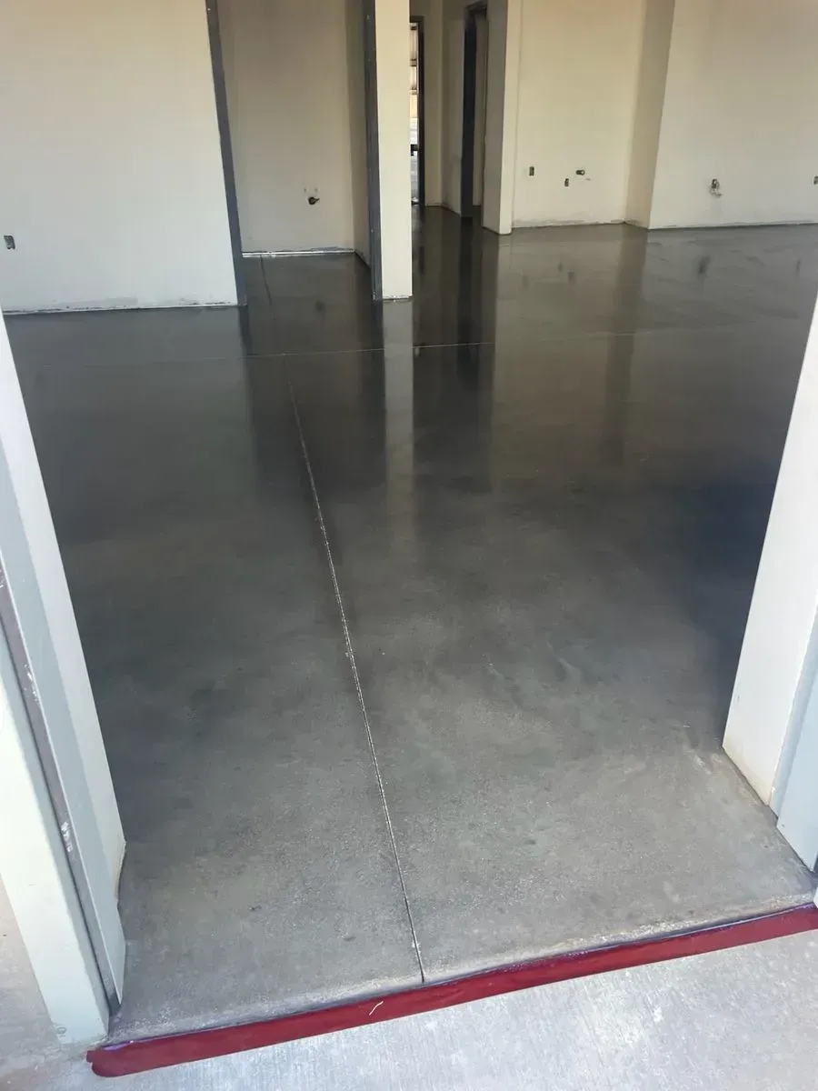 Polished concrete floor in a room, reflecting the light. White walls, a doorway.