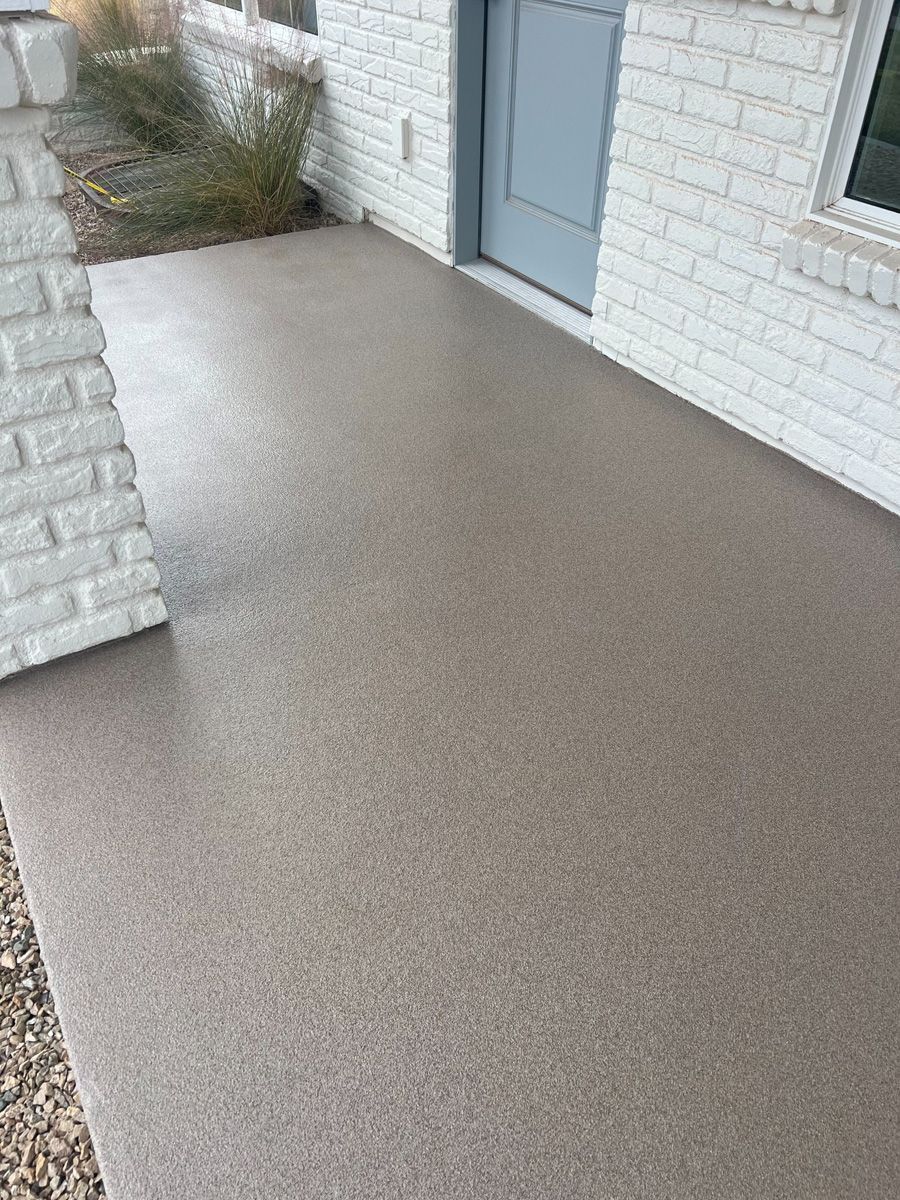 Concrete front porch with a light brown speckled finish next to a white brick wall and a blue door.