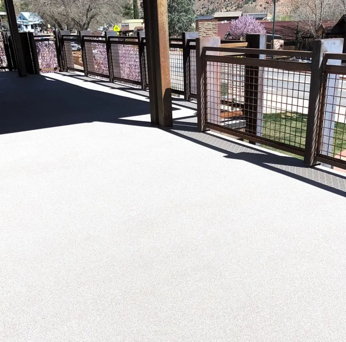 A light gray, textured patio with metal fencing and a wooden support beam, outdoors.