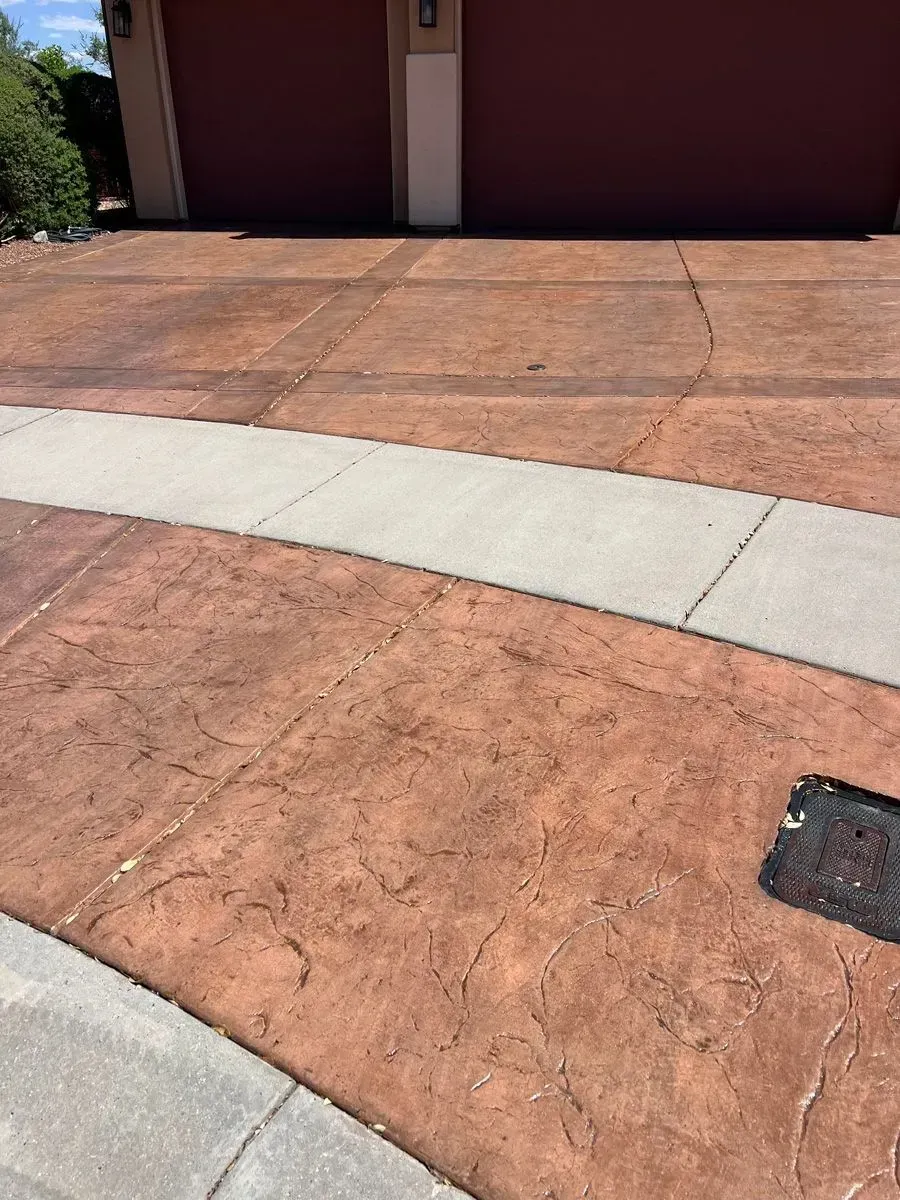 Driveway and sidewalk, colored reddish-brown and gray, leading to a garage with red doors.