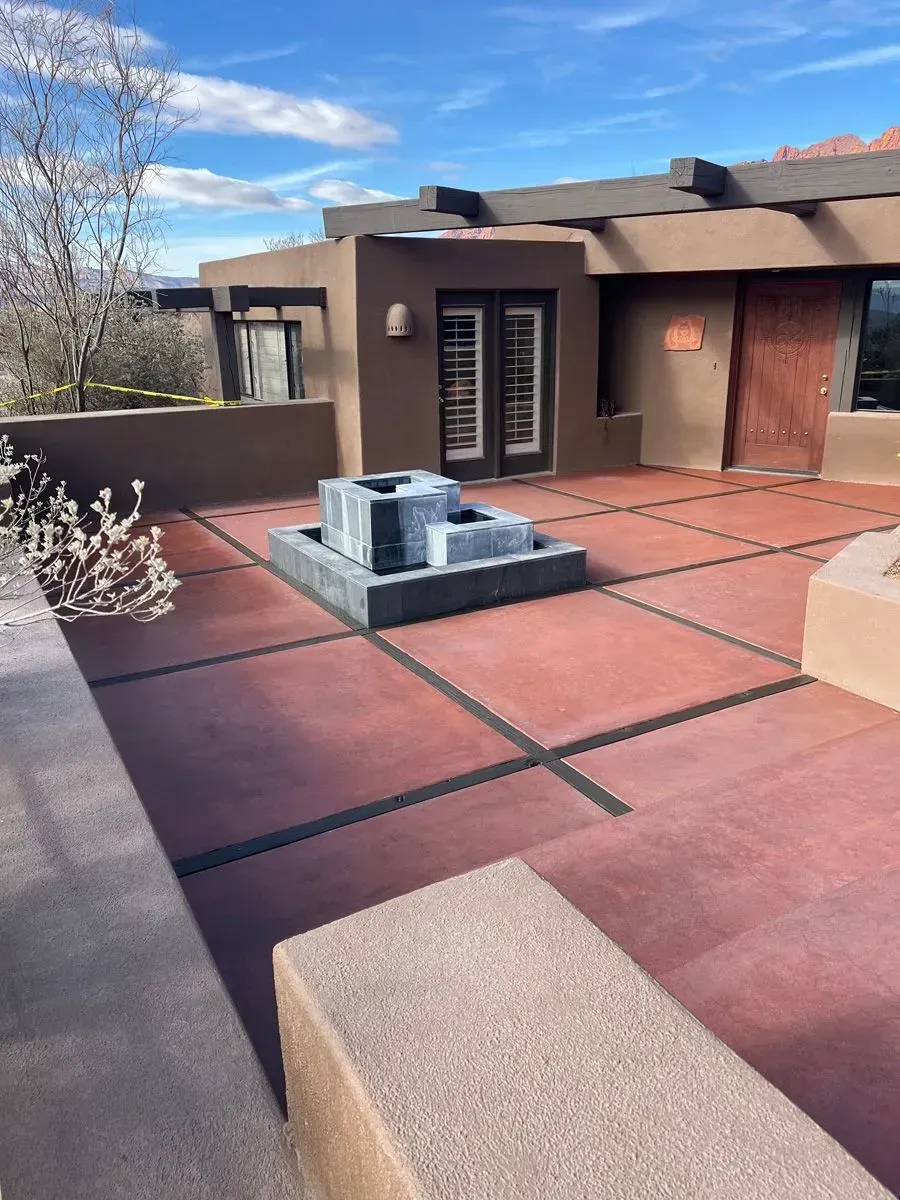 Red-tiled patio with a water fountain, surrounded by a brown adobe-style building. Sunny day.