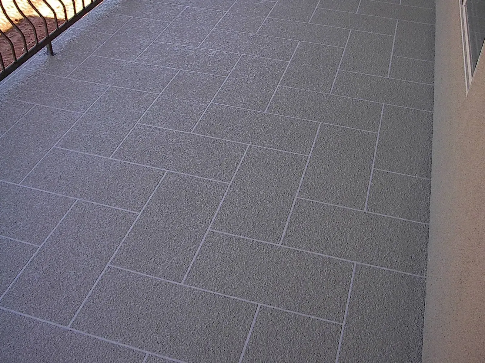 Gray tiled patio with a black railing and a beige wall.