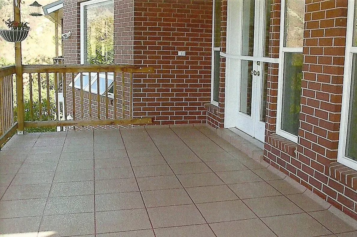 Brown tiled deck with wooden railing, brick wall, and white door.