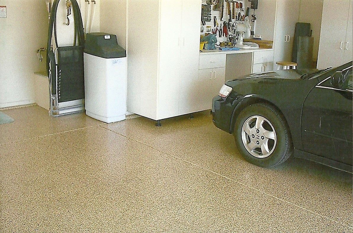 Garage with a speckled floor, a car parked on the right, and storage units and equipment on the left.