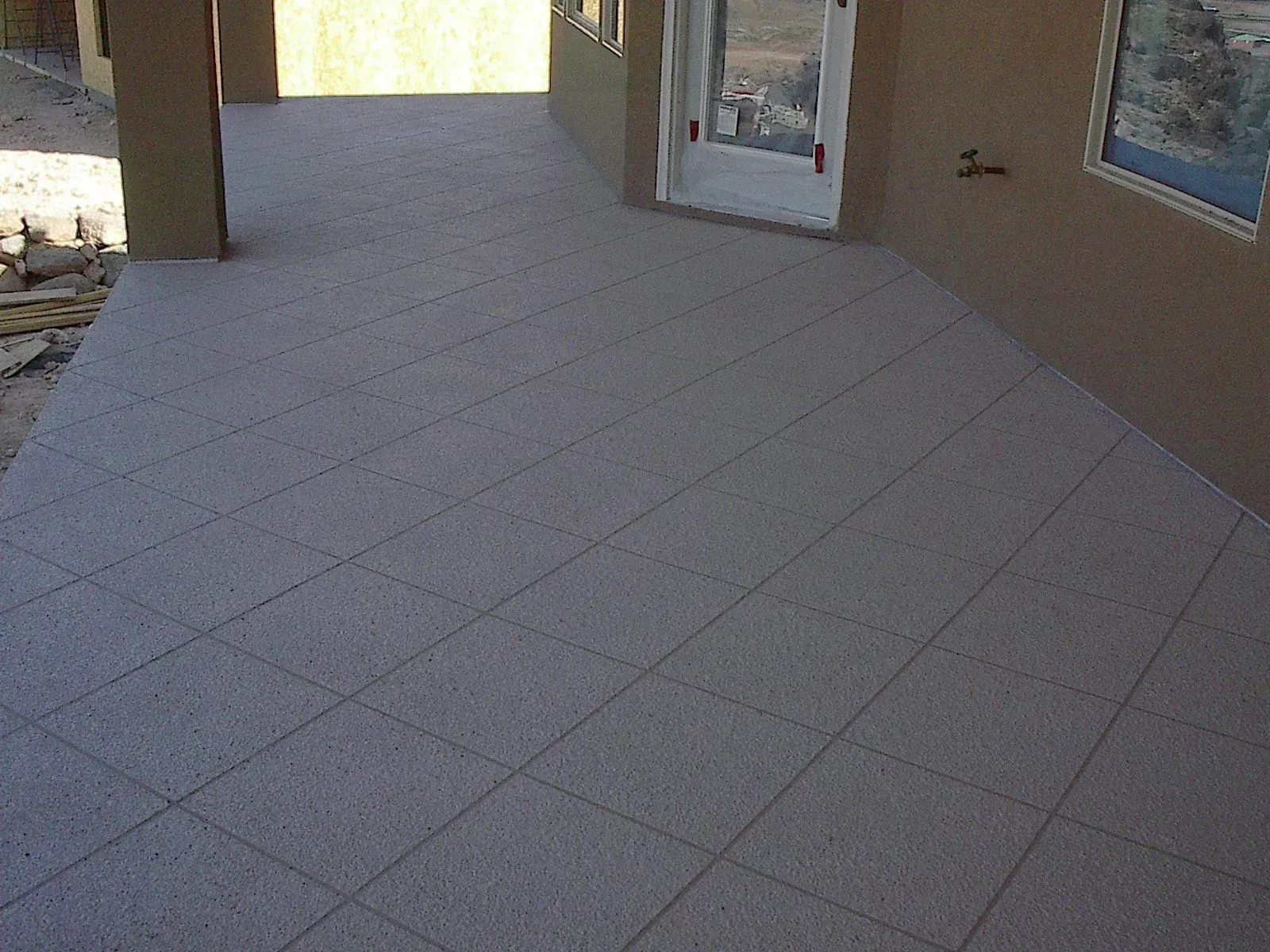 Covered outdoor patio with gray tile, neutral walls, and a door.
