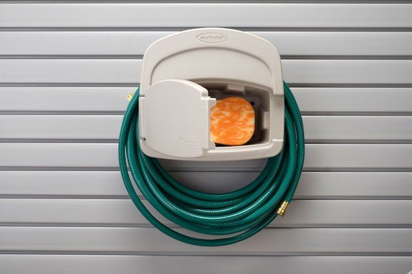 A green hose is hanging from a white holder on a wall.