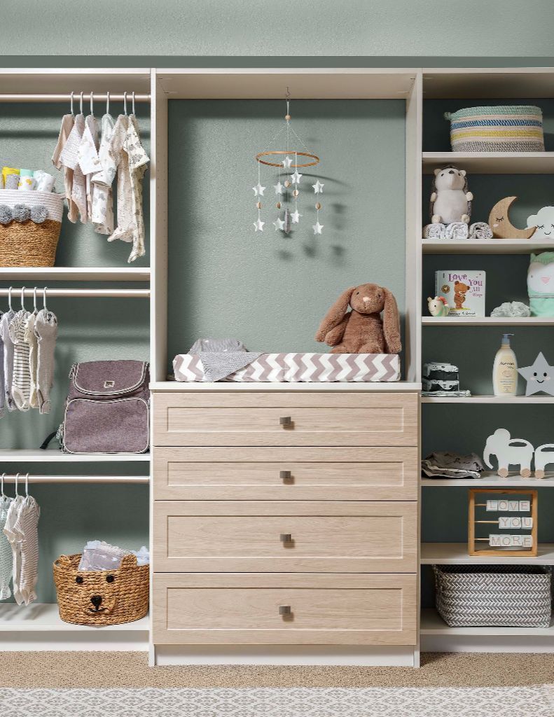 Baby nursery closet with changing table and shelves filled with clothes and toys.