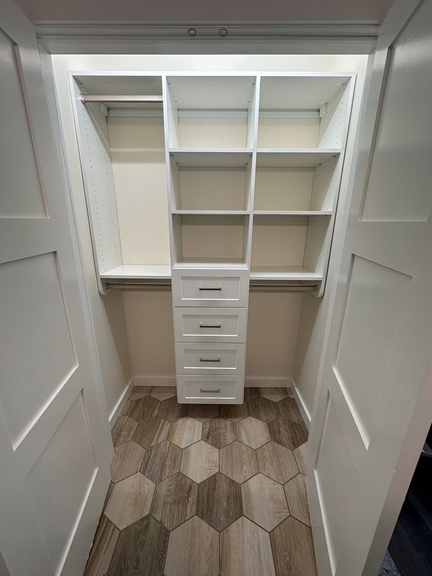 A walk in closet with white shelves and drawers and a wooden floor.