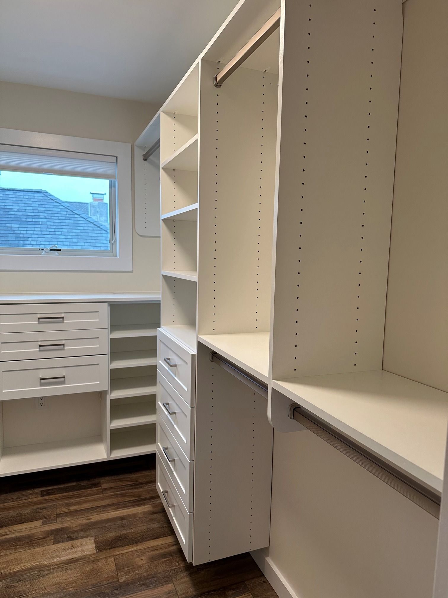A walk in closet with white shelves , drawers , and a window.