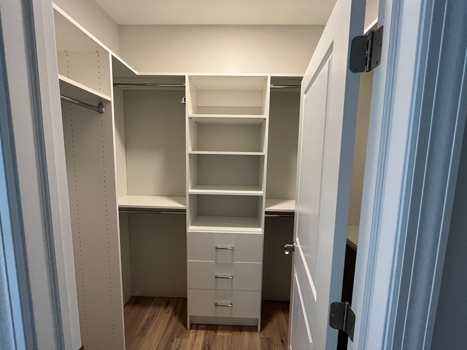 A walk in closet with white shelves and drawers in a bedroom.