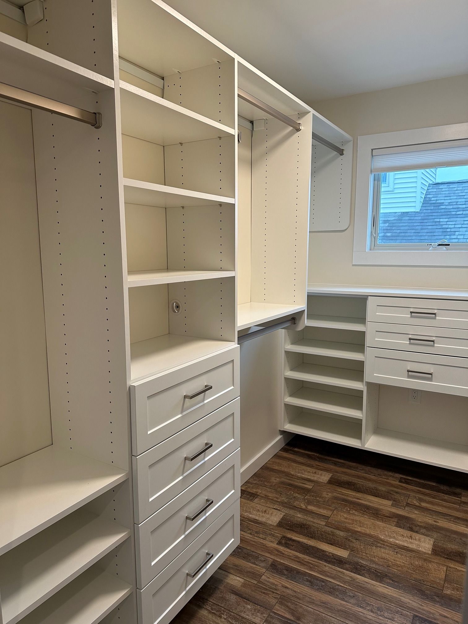 A walk in closet with white shelves and drawers and a window.