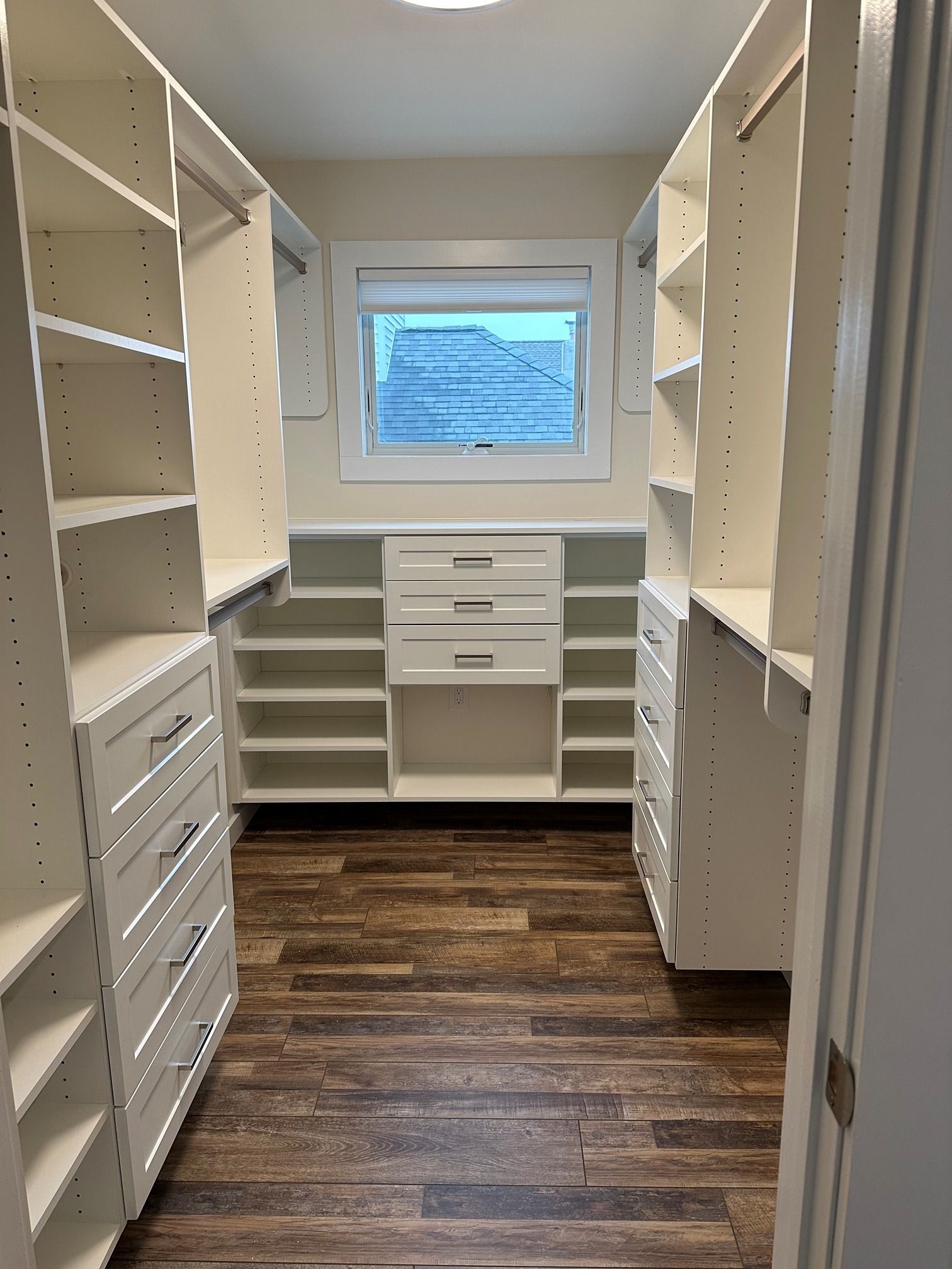 A walk in closet with lots of shelves and drawers and a window.
