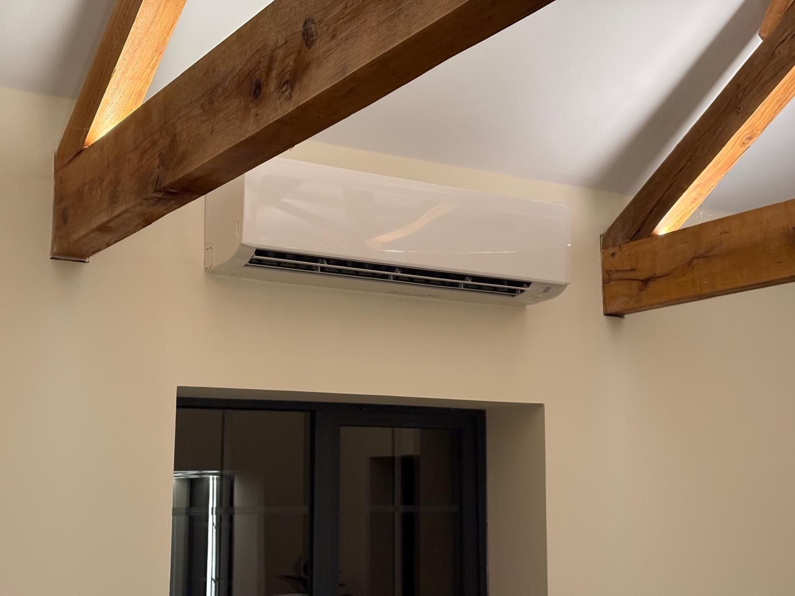 Air conditioner unit on beige wall, wooden beams overhead.