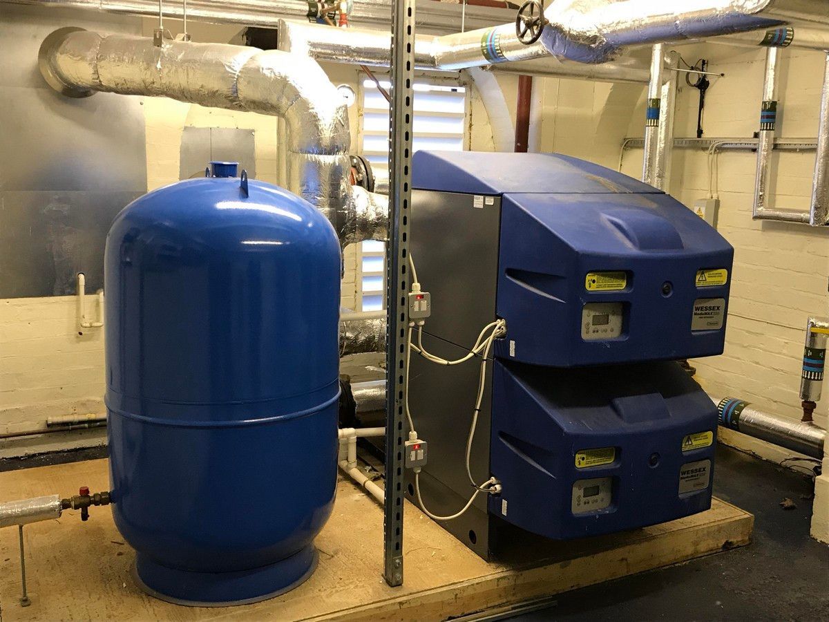 Blue water tank and industrial heater in a mechanical room, pipes and ductwork visible.
