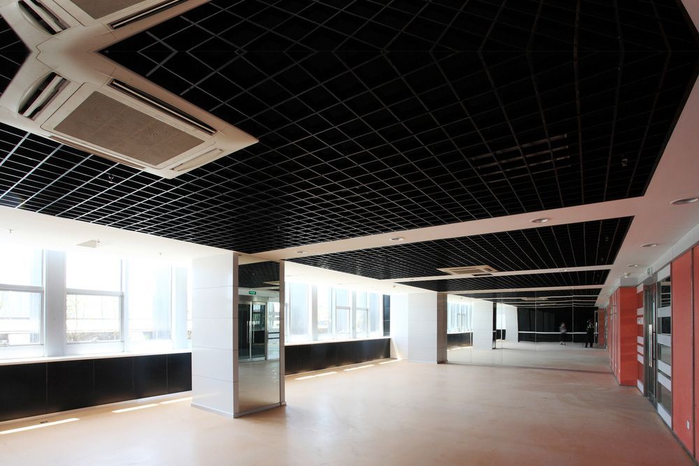 Empty commercial space with black grid ceiling, white pillars, and large windows.