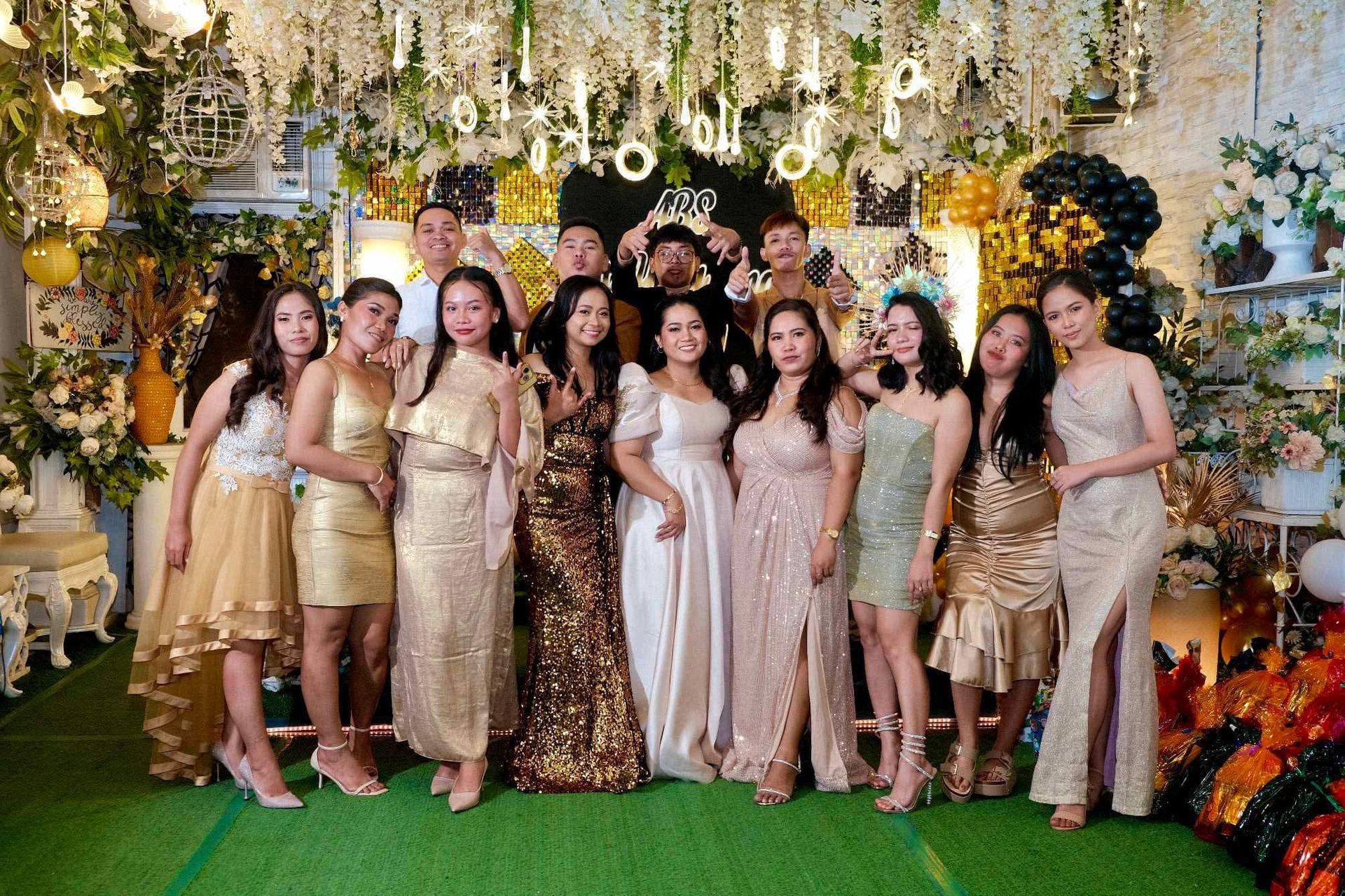 Group of people posing for a photo. They're wearing formal attire in a decorated setting with floral accents.