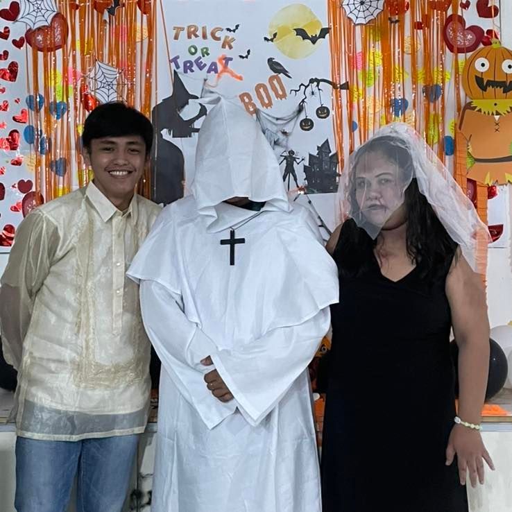 Three people in Halloween costumes posing in front of decorations. 