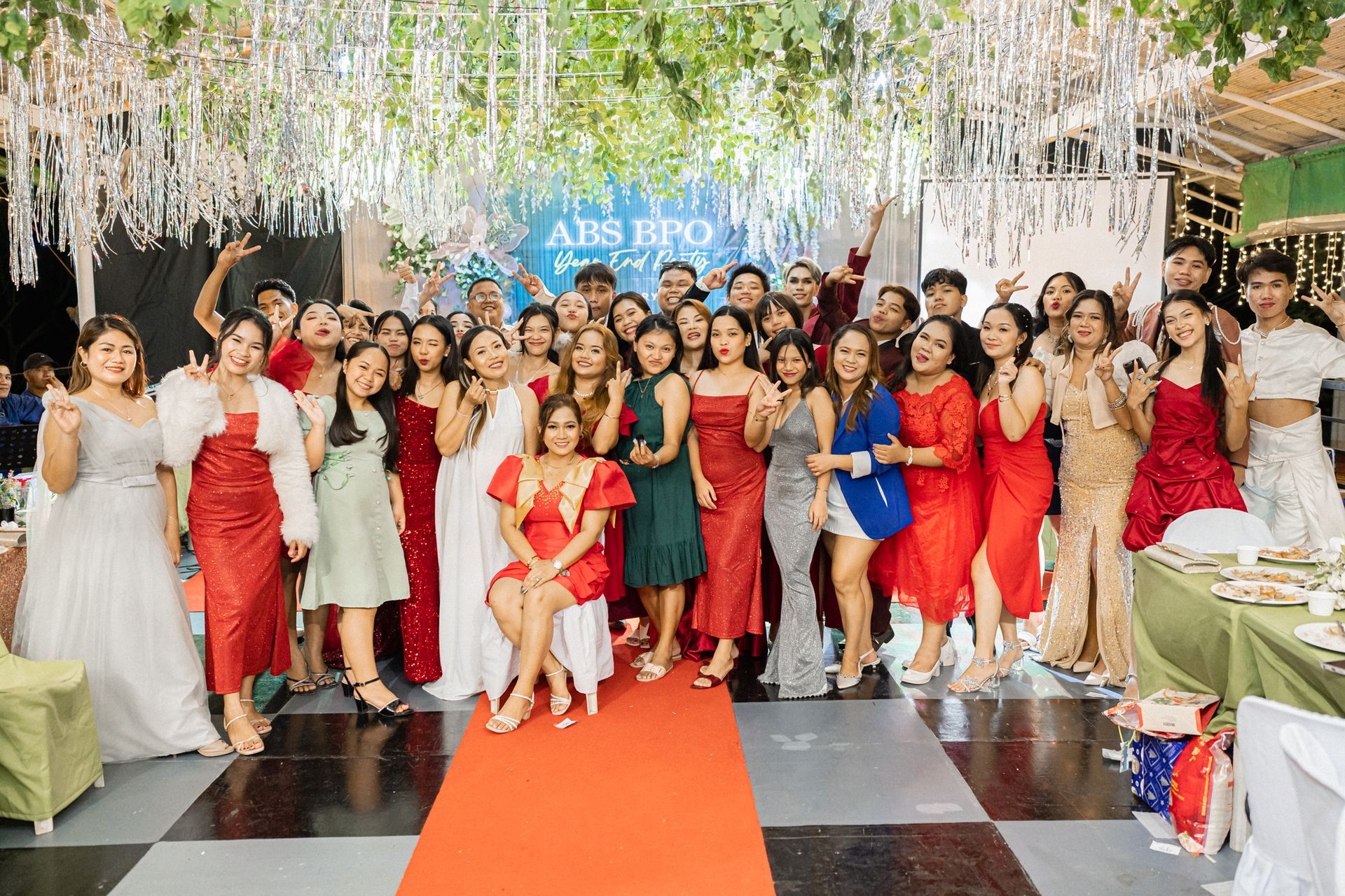 Group of people in formal attire pose for a photo at a decorated event with a red carpet and a sign.