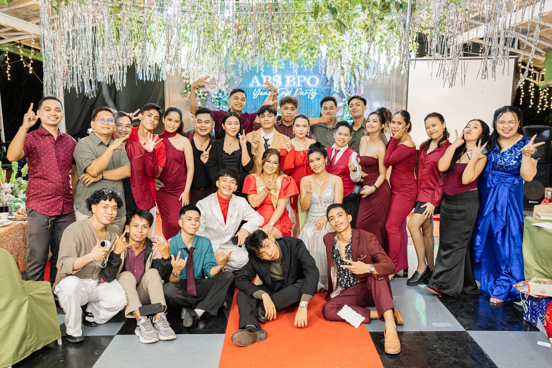 Group photo at a party; people posing with smiles. Decorations include silver tinsel and greenery.