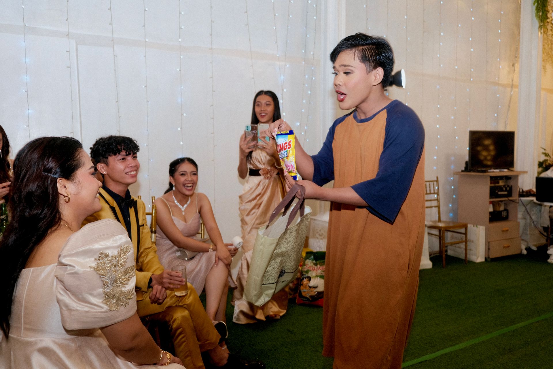 Person gesturing with a treat in front of a group. Indoor event with formal attire.
