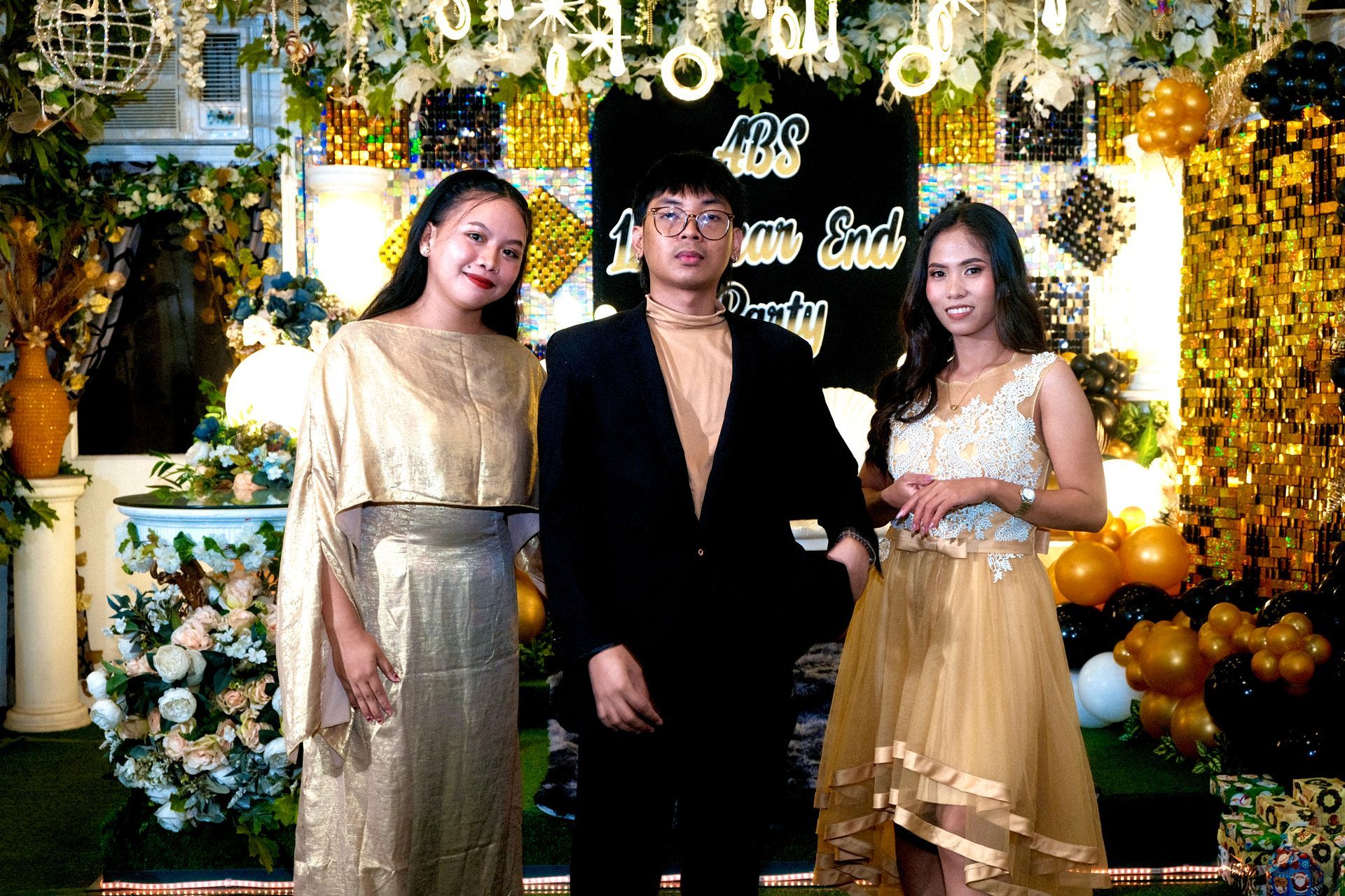 Three people pose at a party with gold and black decorations.