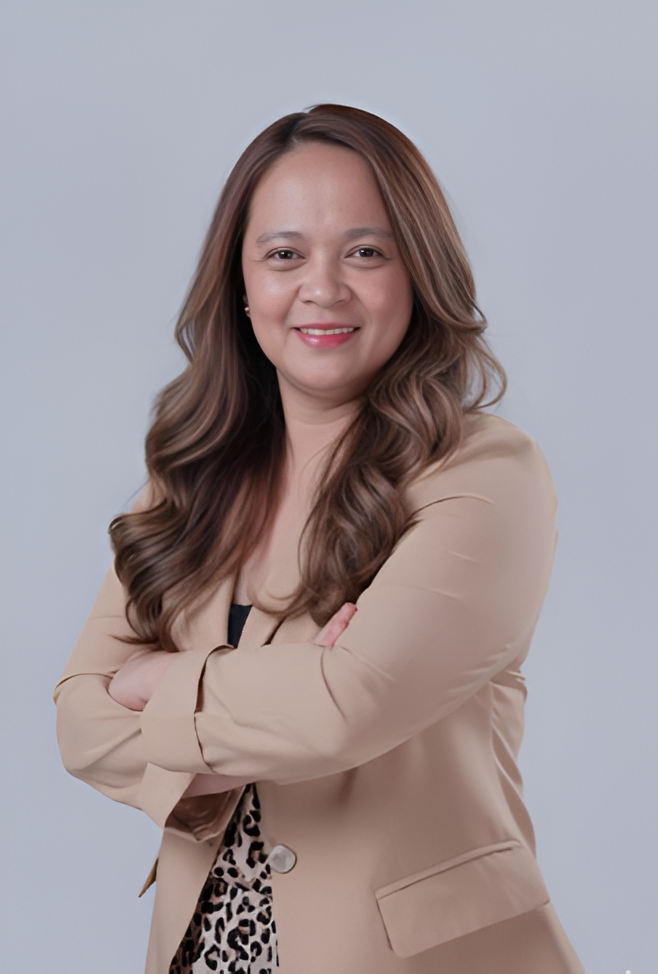 Woman with arms crossed, smiling. Wearing tan blazer over a printed top. Light background.