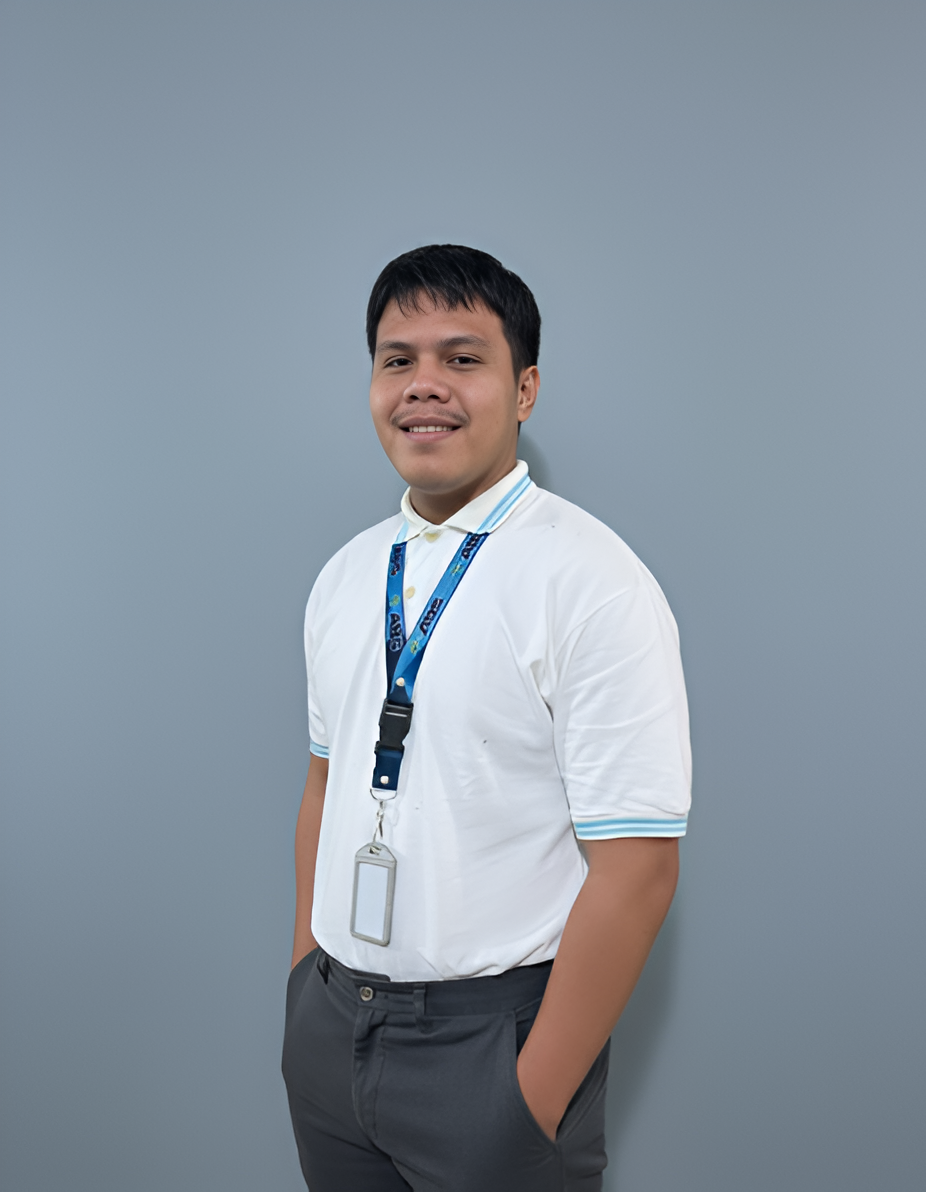 Man in white polo and gray pants, hands in pockets, smiling against a gray wall, wearing ID badge.
