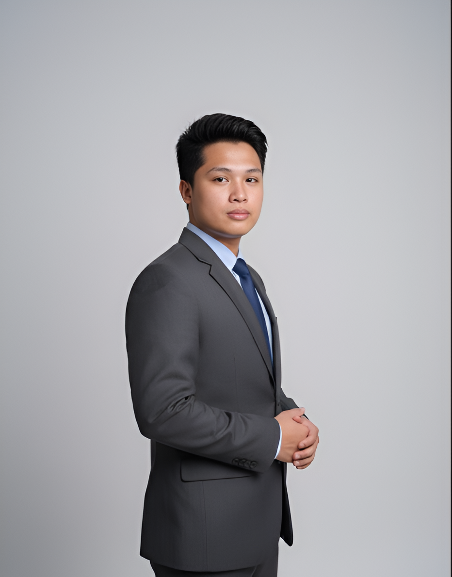 Man in gray suit and blue tie stands against a light gray background, hands clasped.