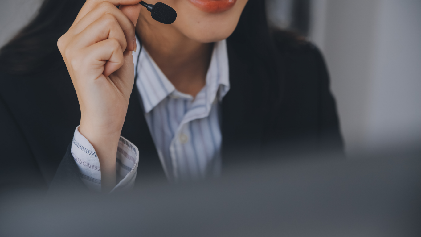 Woman wearing a headset, in a suit, speaking into microphone.
