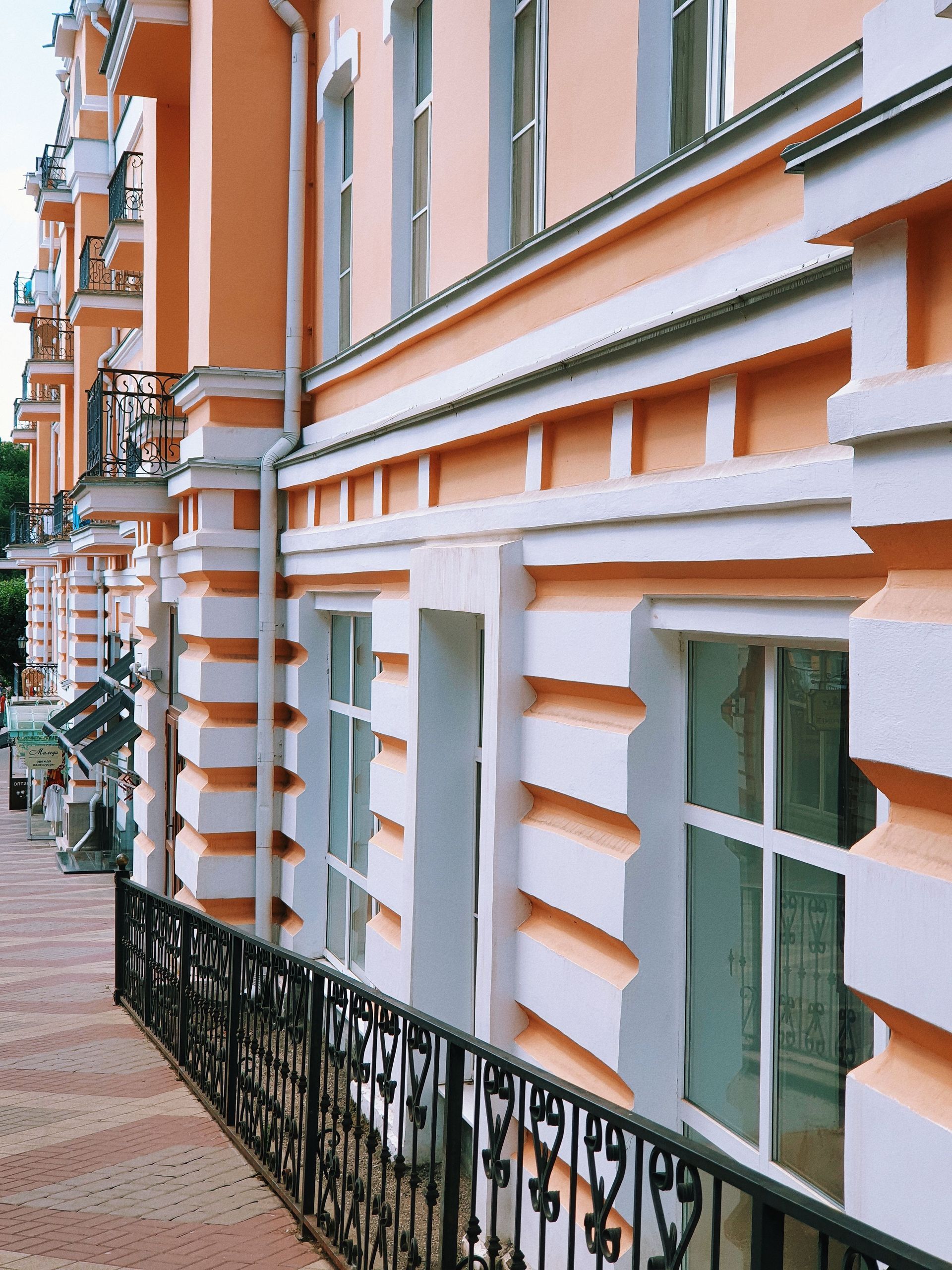 Pastel orange building facade with white trim and black wrought-iron railing along a brick sidewalk