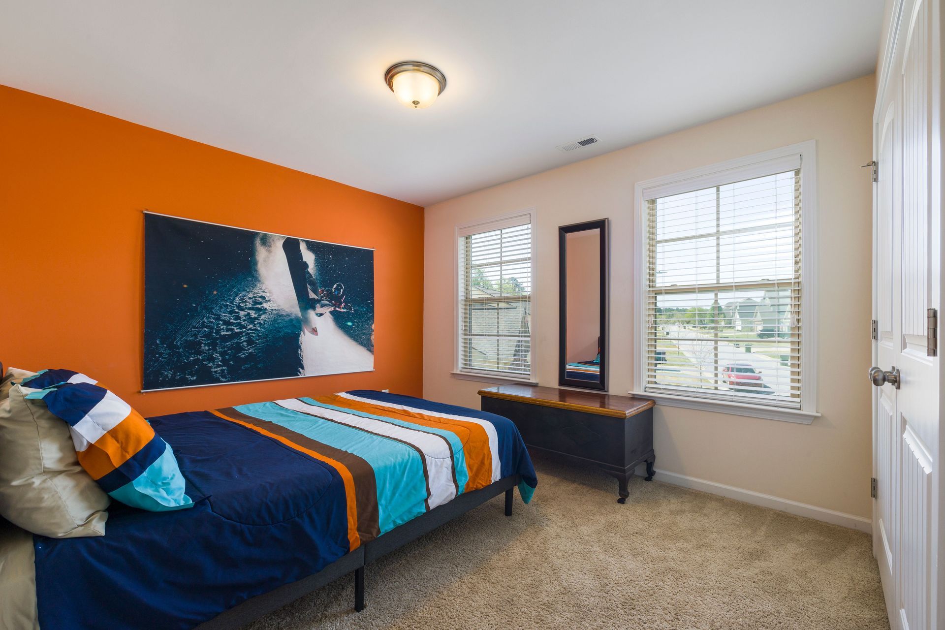 Small bedroom with navy bed, orange accent wall, desk, and windows with blinds