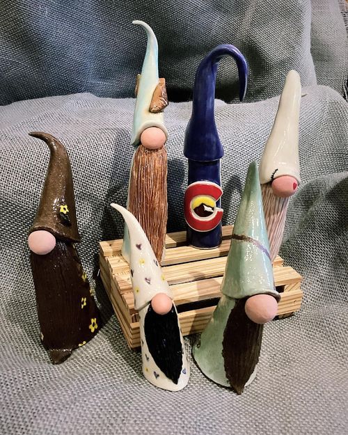 Seven small hand-painted cone-shaped figurines on a tiny wooden pallet against a gray fabric background.