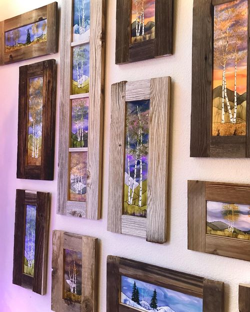 Assorted rustic framed landscape paintings arranged on a white gallery wall
