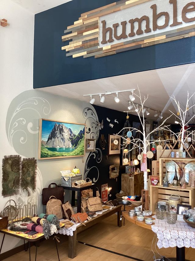 Boutique shop interior with handmade crafts, tables of decor, and a “humble” sign above the entrance