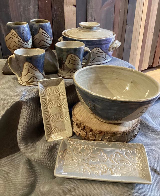 Blue-and-cream ceramic pottery set with cups, bowls, and plates on a textured display cloth