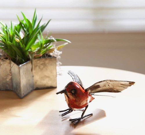 Small red bird figurine with spread wings on a white table, beside a potted succulent