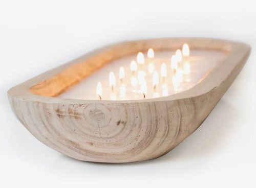 Wooden bowl-shaped candle holder with several lit white candles on a white background