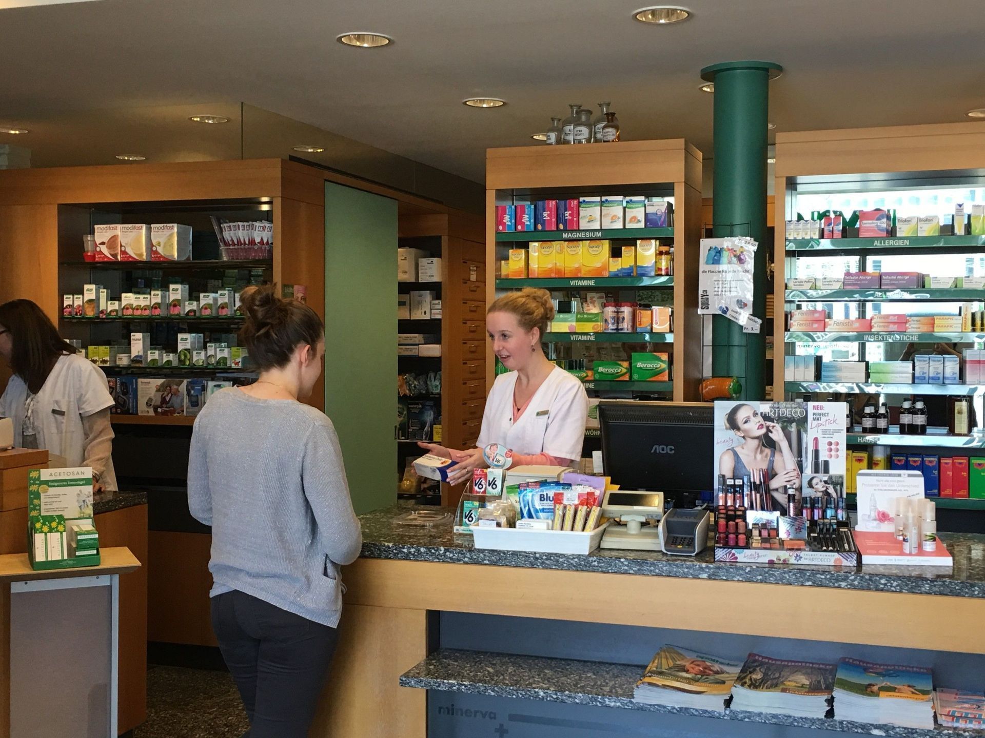 Eine Frau steht an einem Tresen in einer Apotheke und unterhält sich mit einer anderen Frau