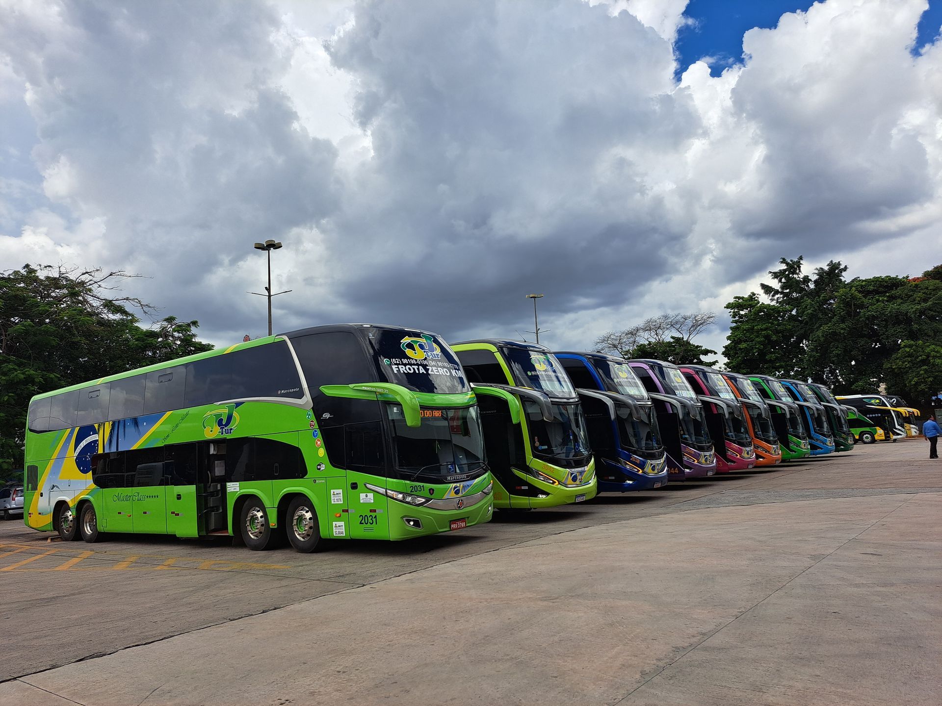 Fila de ônibus da JJTur de diferentes cores estacionados