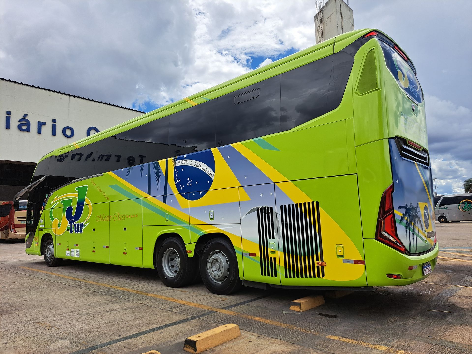 Um ônibus verde limão da JJTur com visão da lateral e parte da traseira