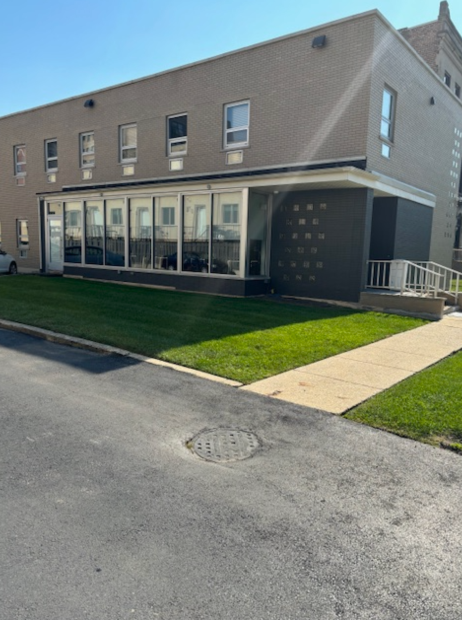 A large building with a lot of windows is sitting next to a sidewalk.