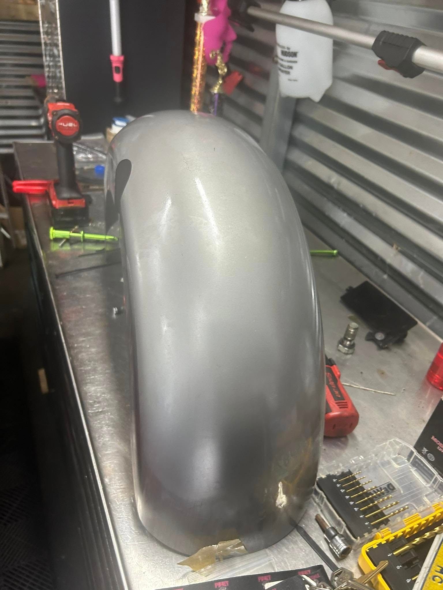 Silver motorcycle fender on a metal workbench with tools in the background.