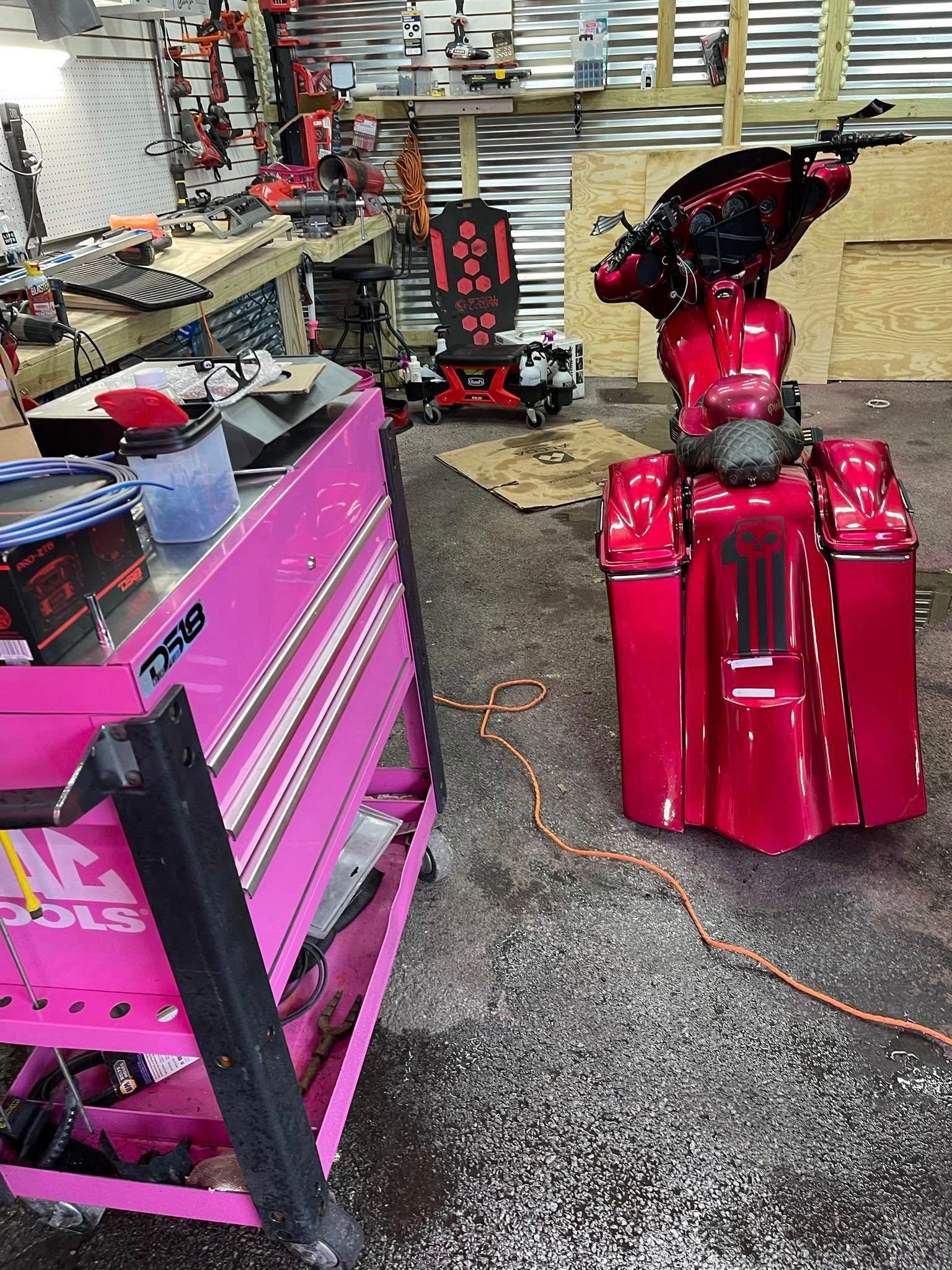Pink motorcycle next to a pink tool cart in a workshop.