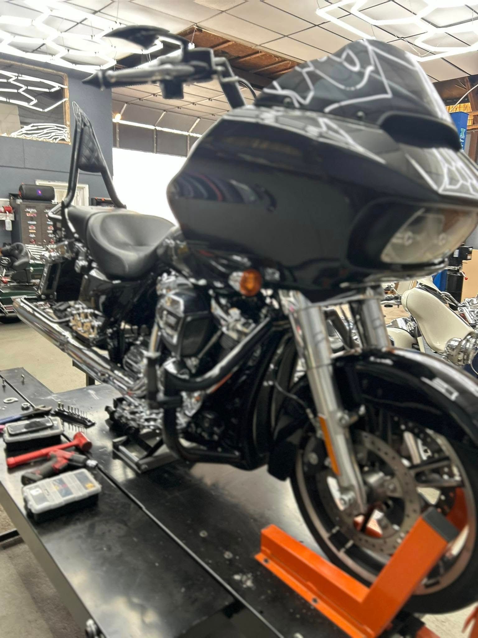 Black Harley-Davidson motorcycle on a lift in a shop, orange lift supports, tools on the table.