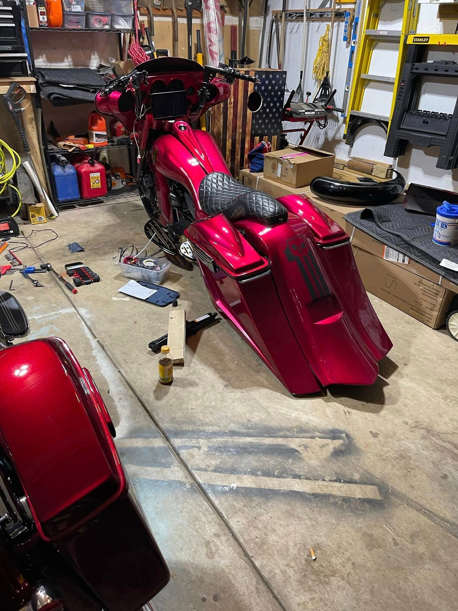 A custom red motorcycle in a garage. Tail is lowered and extended, black seat. Tools and boxes surround it.