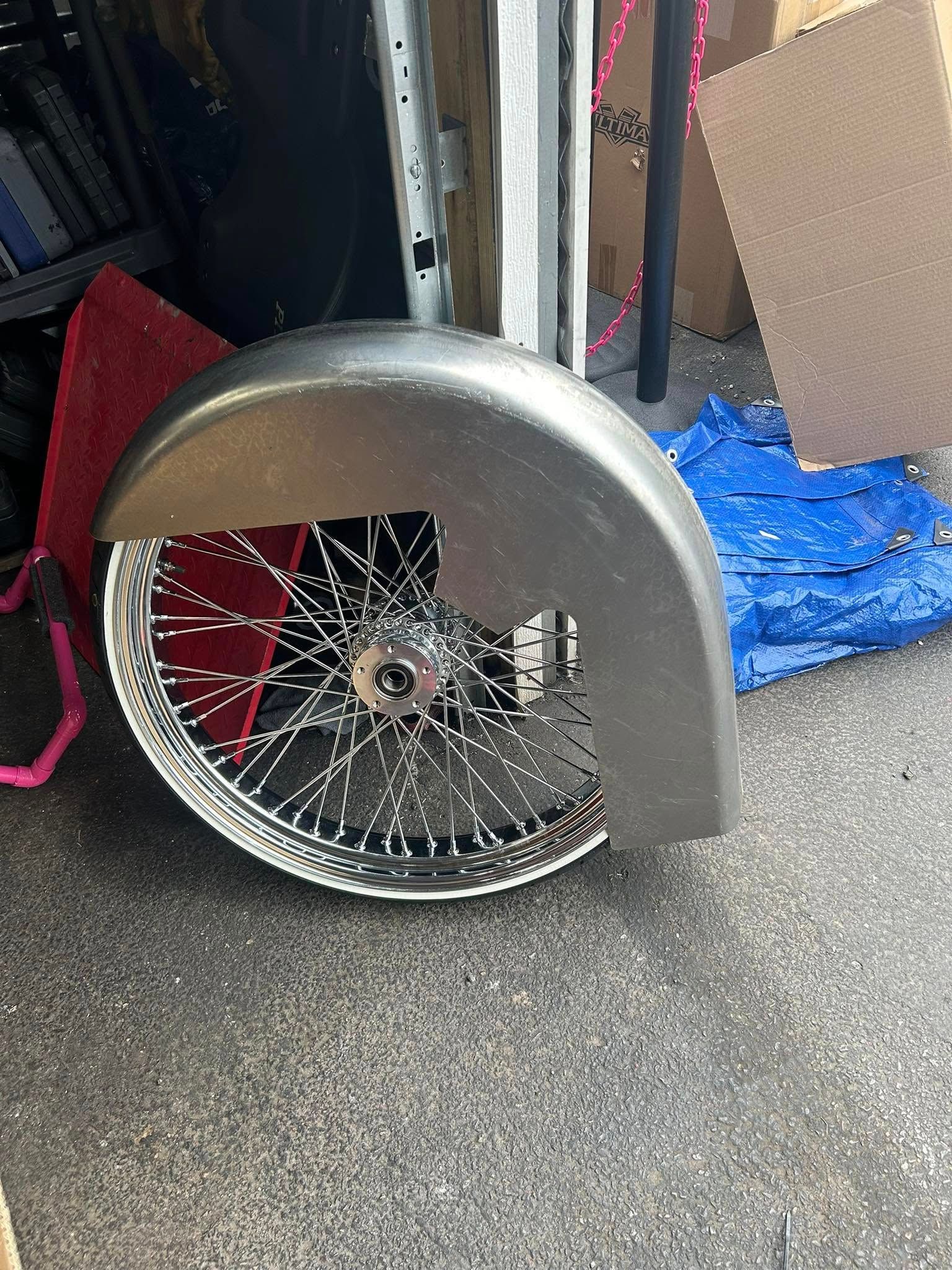 Metal motorcycle fender with wire-spoked wheel, outdoors, unfinished.
