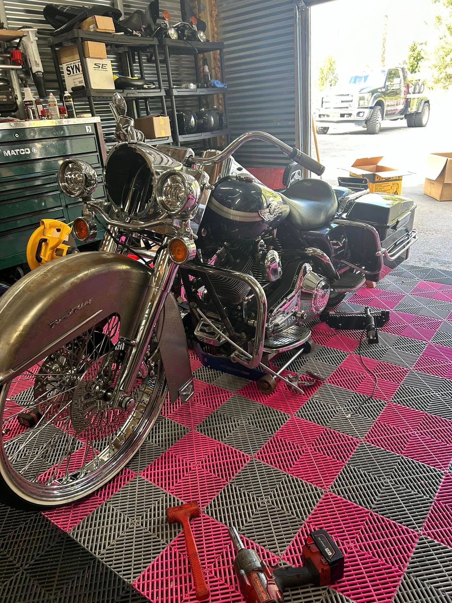 Chrome motorcycle parts on a pink and gray checkered floor in a workshop.